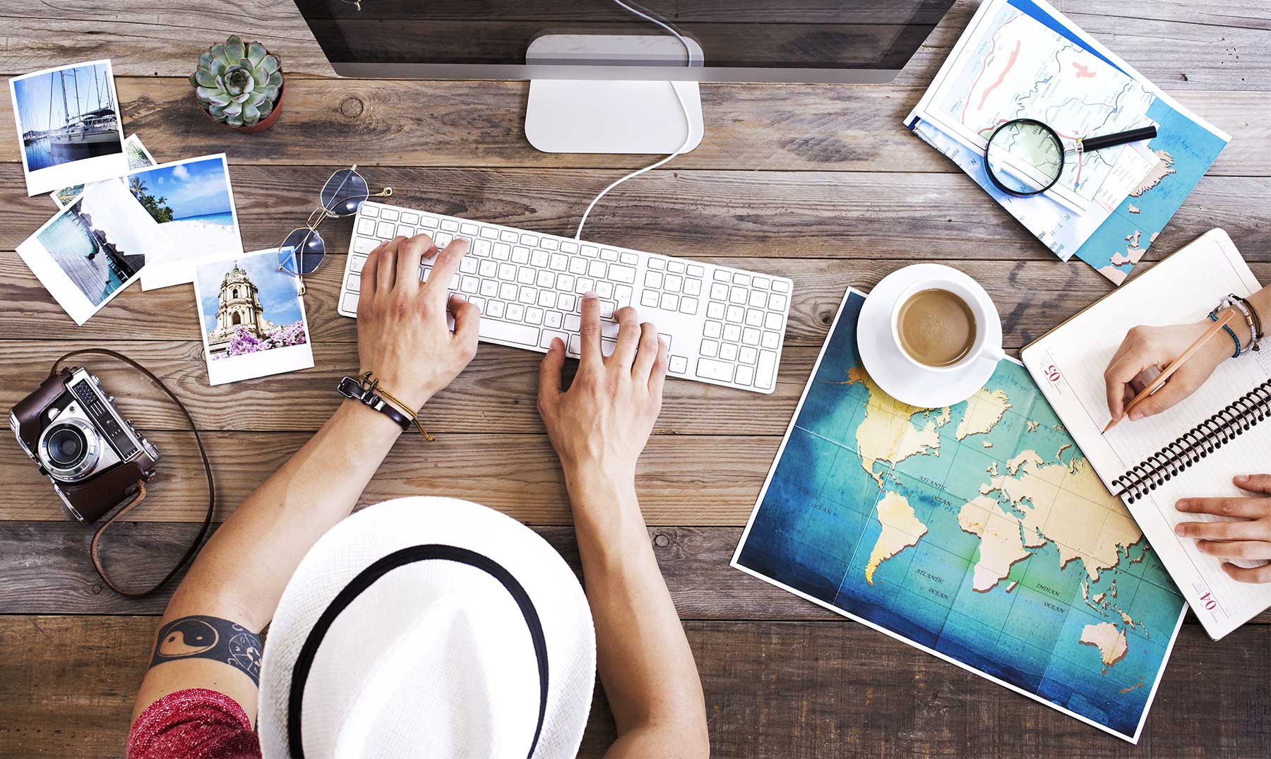 Persona planificando inversiones en hoteles y turismo desde una oficina, con mapas, fotografías de viajes, cámara y computadora sobre la mesa, representando la guía completa para un futuro rentable en la industria turística.